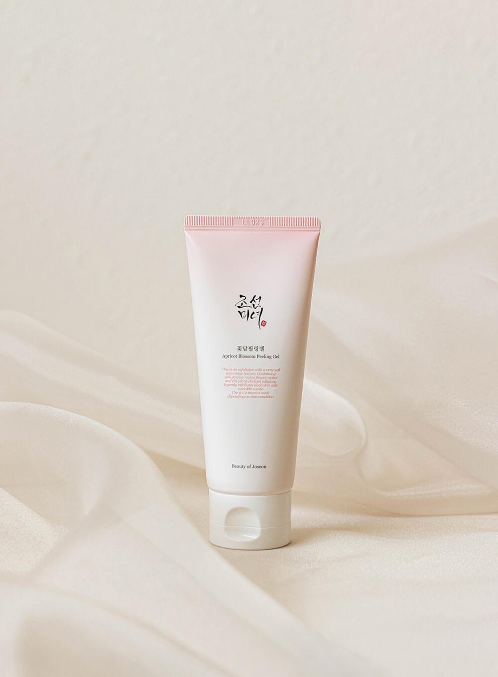 100ml tube of Beauty of Joseon Apricot Blossom Peeling Gel, a Korean skincare product with apricot blossom water for gentle exfoliation against a white flow backdrop