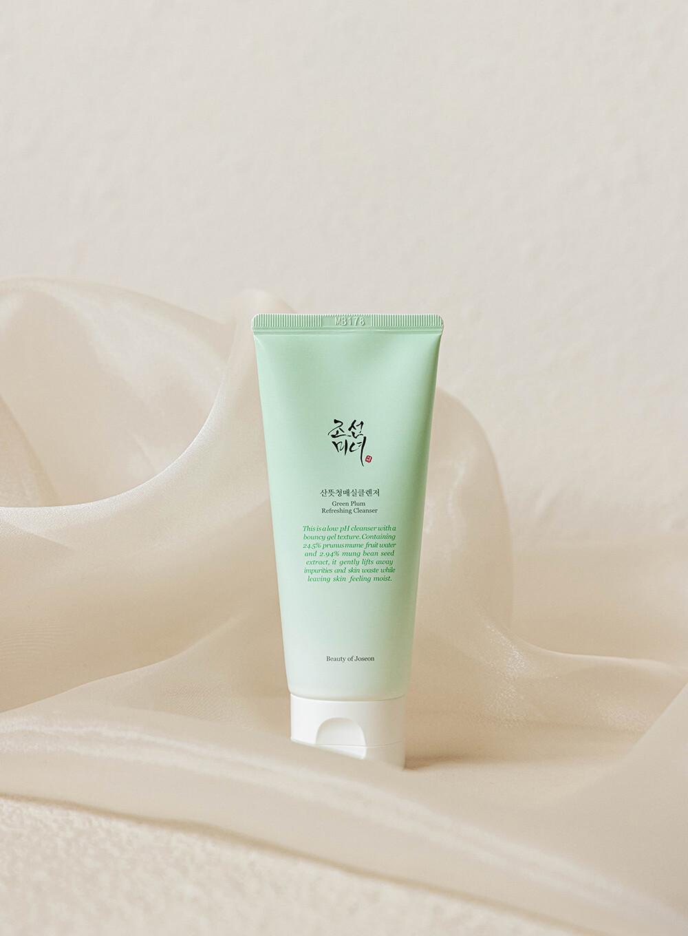 100ml green tube of Beauty of Joseon Green Plum Refreshing Cleanser, a lightweight gel cleanser with green plum and mung bean for gentle cleansing and hydration against a white flowy backdrop