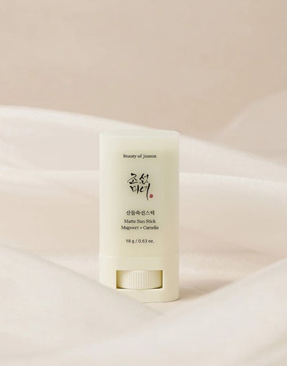 Travel-friendly, 18g stick sunscreen by Beauty of Joseon with mugwort and camellia for shine control and SPF protection against a white flowy backdrop