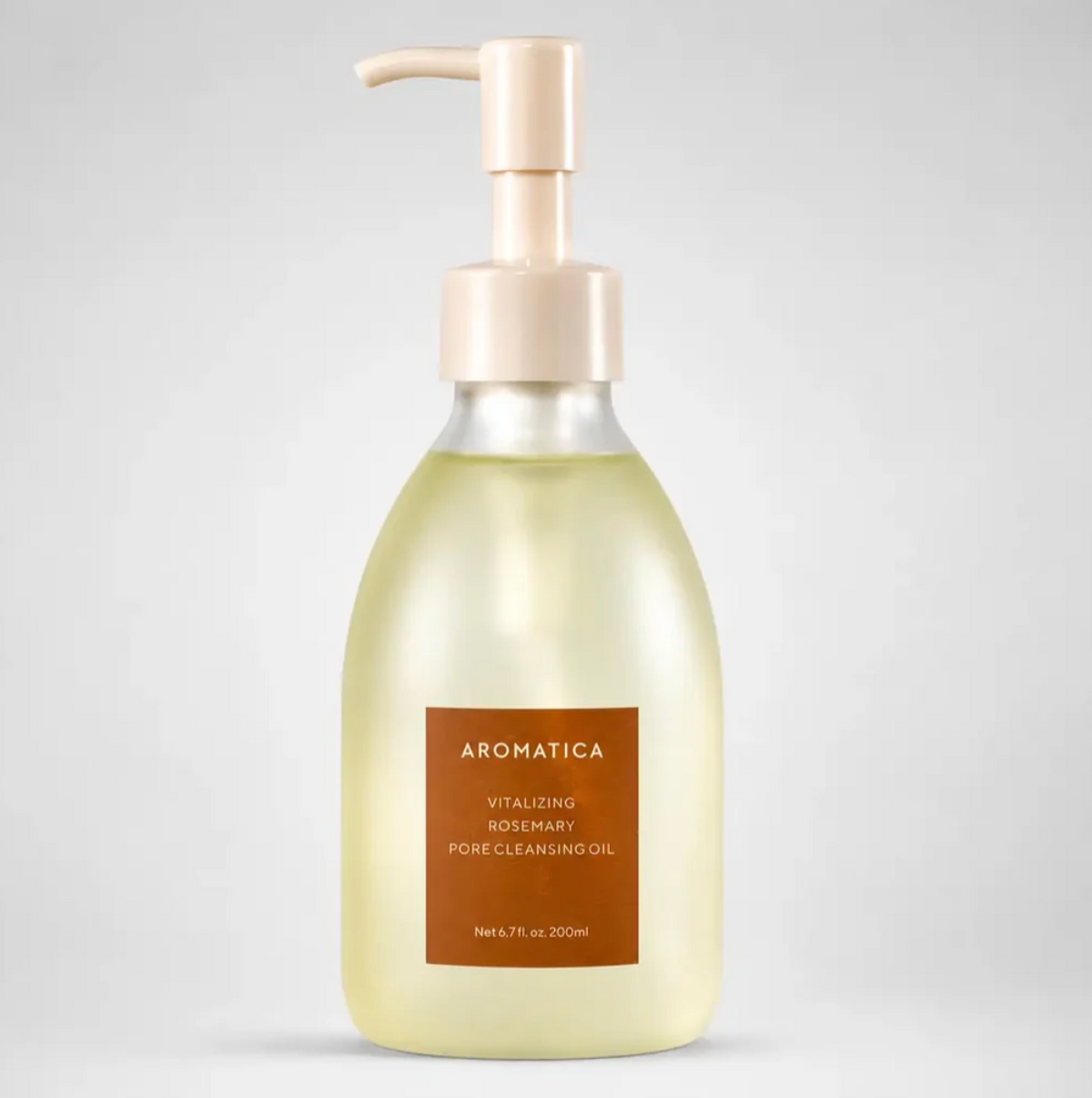 A bottle of Aromatica Vitalizing Rosemary Pore Cleansing Oil on a light gray background. The bottle is made of frosted glass showing a pale yellow oil inside, with a beige pump dispenser and a brown label.