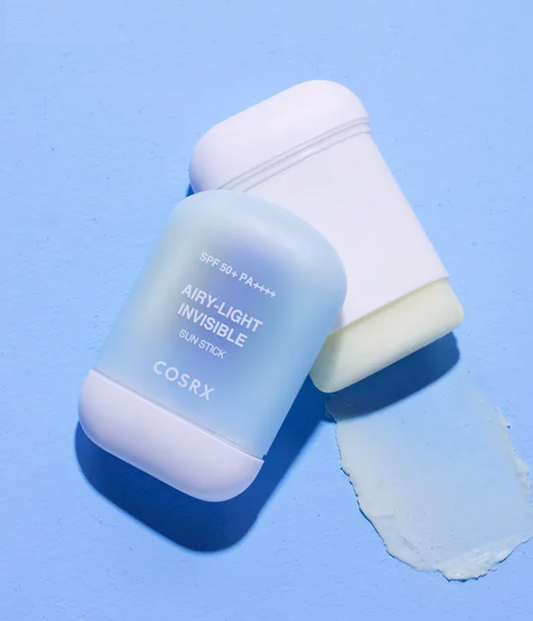 COSRX Airy-Light Invisible Sun Stick SPF 50+ PA++++ in a frosted light blue stick container with a white cap, shown next to a smear of the pale blue cream on a solid blue background.