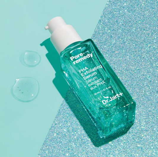 A bottle of Dr. Jart+ Pore-remedy PHA Exfoliating Serum lies diagonally on a split background of solid mint green and silver glitter, with two clear liquid droplets on the left.