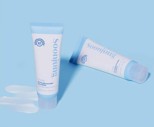 Two white tubes with light blue caps, displayed on a solid light blue background with a small smear of white balm in the foreground.