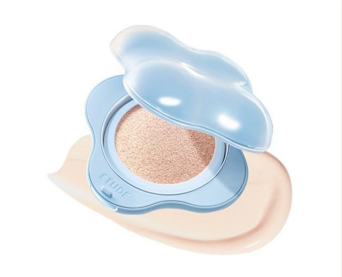 An open ETUDE Hydro Grip Cushion Foundation compact with a light blue flower-shaped case, showing the beige foundation powder inside and a smear of the beige foundation underneath on a white background.