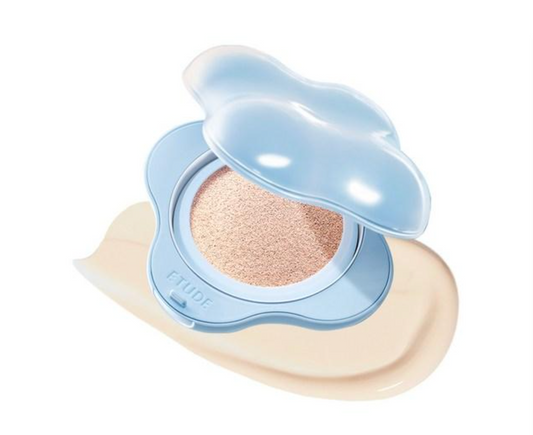 A cloud-shaped cushion foundation compact by CYUDE, shown open with the light blue lid propped up, revealing a beige-toned powder cushion. A smear of the beige foundation product is visible beneath the compact on a clean white background.
