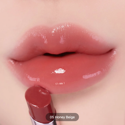 Close-up of glossy lips wearing a warm nude lip color, with a lipstick bullet labeled '05 Honey Beige' touching the lower lip.