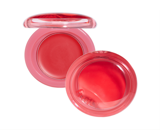 A pink cosmetic compact with a translucent lid, shown open to reveal a bright coral-red cream product inside, on a plain white background.