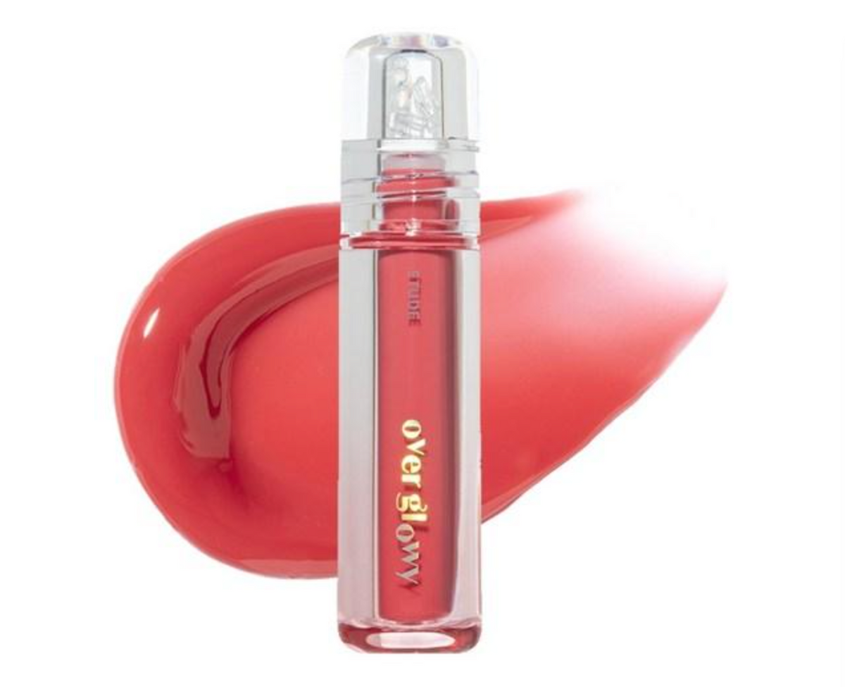 A clear cylindrical bottle of liquid lipstick with gold lettering, positioned in front of a glossy red lipstick smear on a white background.