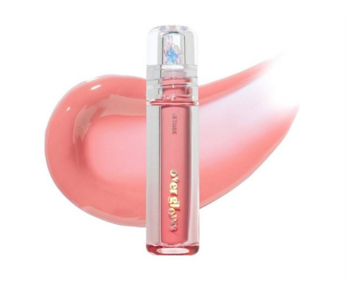 A clear cylindrical bottle of liquid lipstick with pink liquid inside, shown in front of a glossy peach-pink color smear on a white background. 