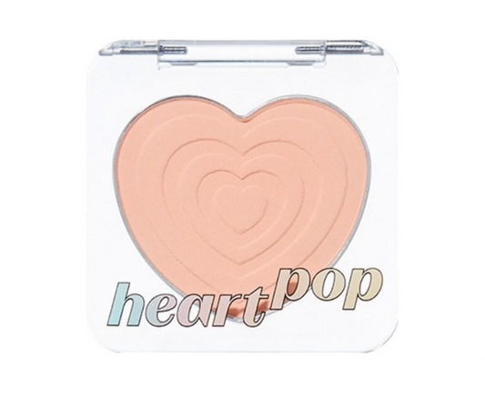 A makeup compact with a clear lid and a large heart-shaped pressed powder in a peachy beige shade. The words 'heart pop' are printed across the lower front of the compact.