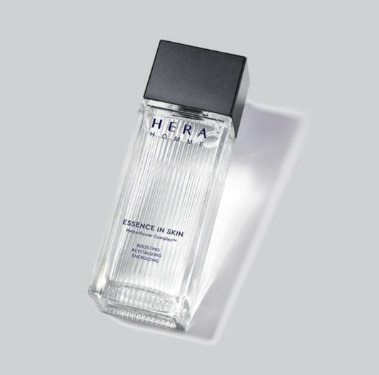 A clear rectangular glass bottle of HERA HOMME Essence in Skin with a matte black cap, shown on a light gray background with a soft shadow.