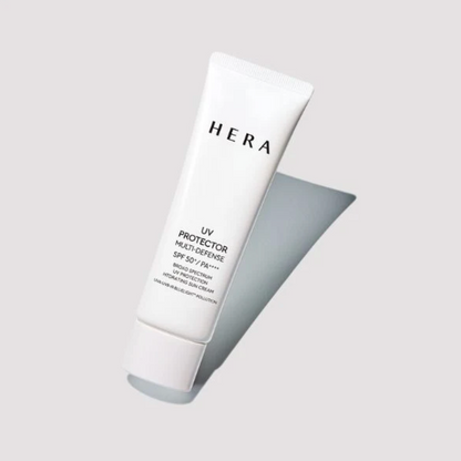 A white squeeze tube of HERA UV Protector Multi-Defense SPF 50+ PA++++ moisturizing sunscreen cream, shown at an angle on a light gray background with a soft shadow.