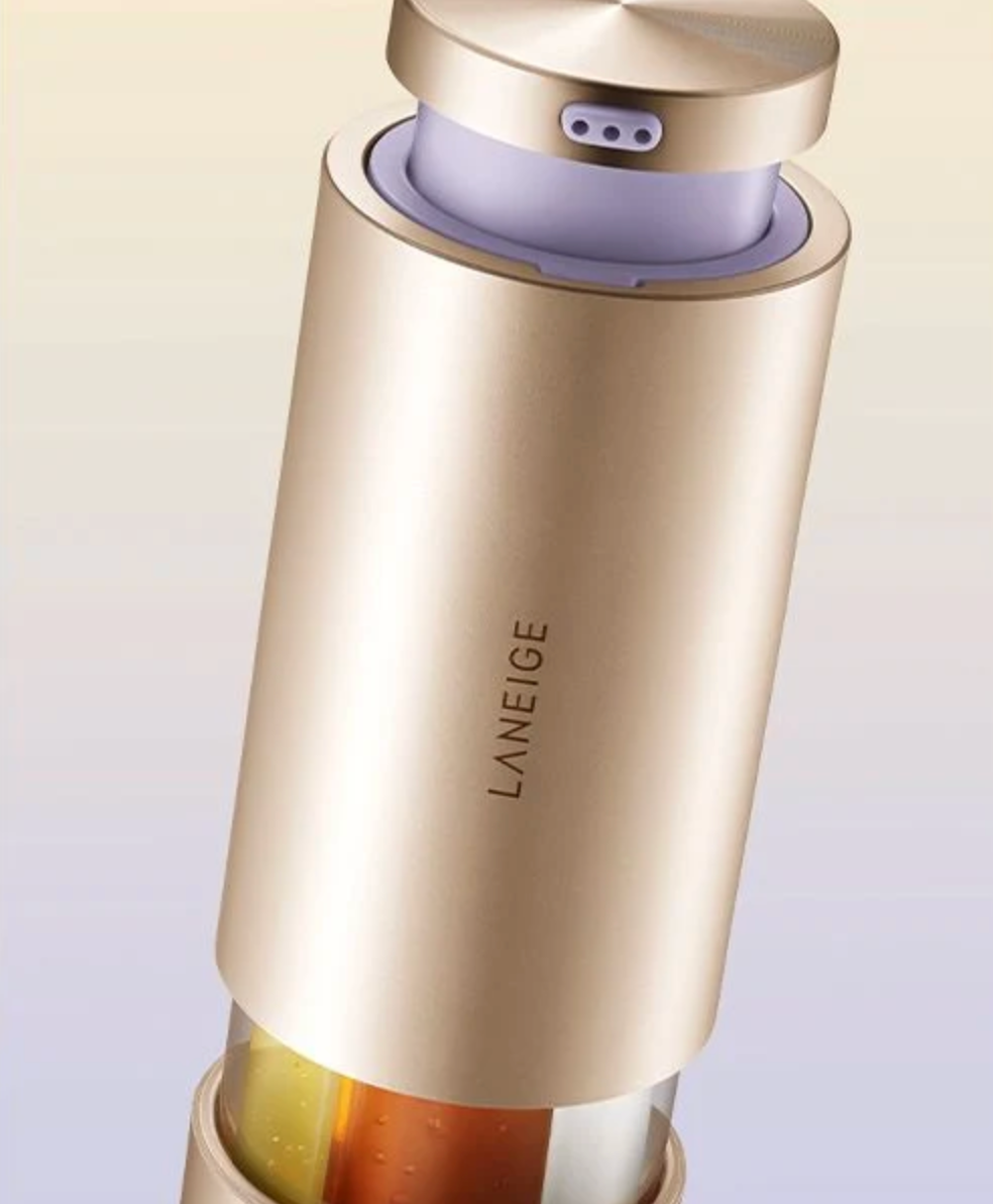 A close-up of a metallic champagne-gold cylindrical device with the brand name 'LANEIGE' printed vertically on the side, set against a soft beige gradient background.