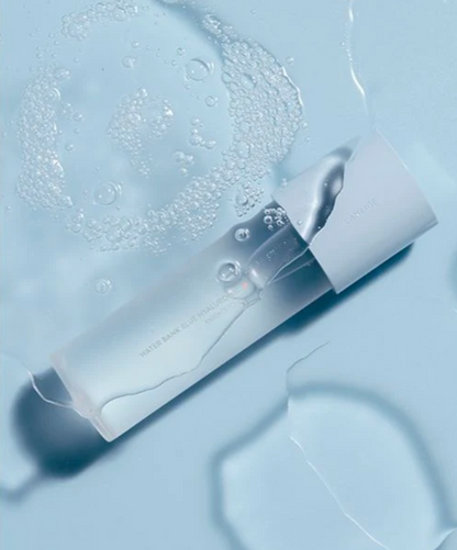 A frosted cylindrical cosmetic bottle with a white cap, partially submerged in clear liquid with visible bubbles, on a pale blue background.