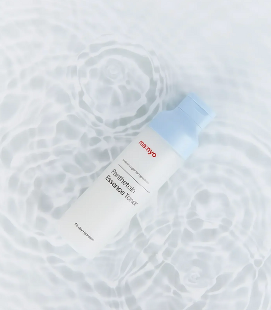 A white bottle of ma:nyo Panthetoin Essence Toner with a light blue cap, placed on a white surface with a water ripple pattern.