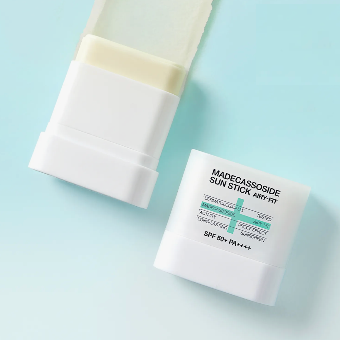 A white Madecassoside Sun Stick Airy-Fit SPF 50+ PA++++ sunscreen stick shown open with the cream-colored stick visible, alongside its white cap, on a light blue background.