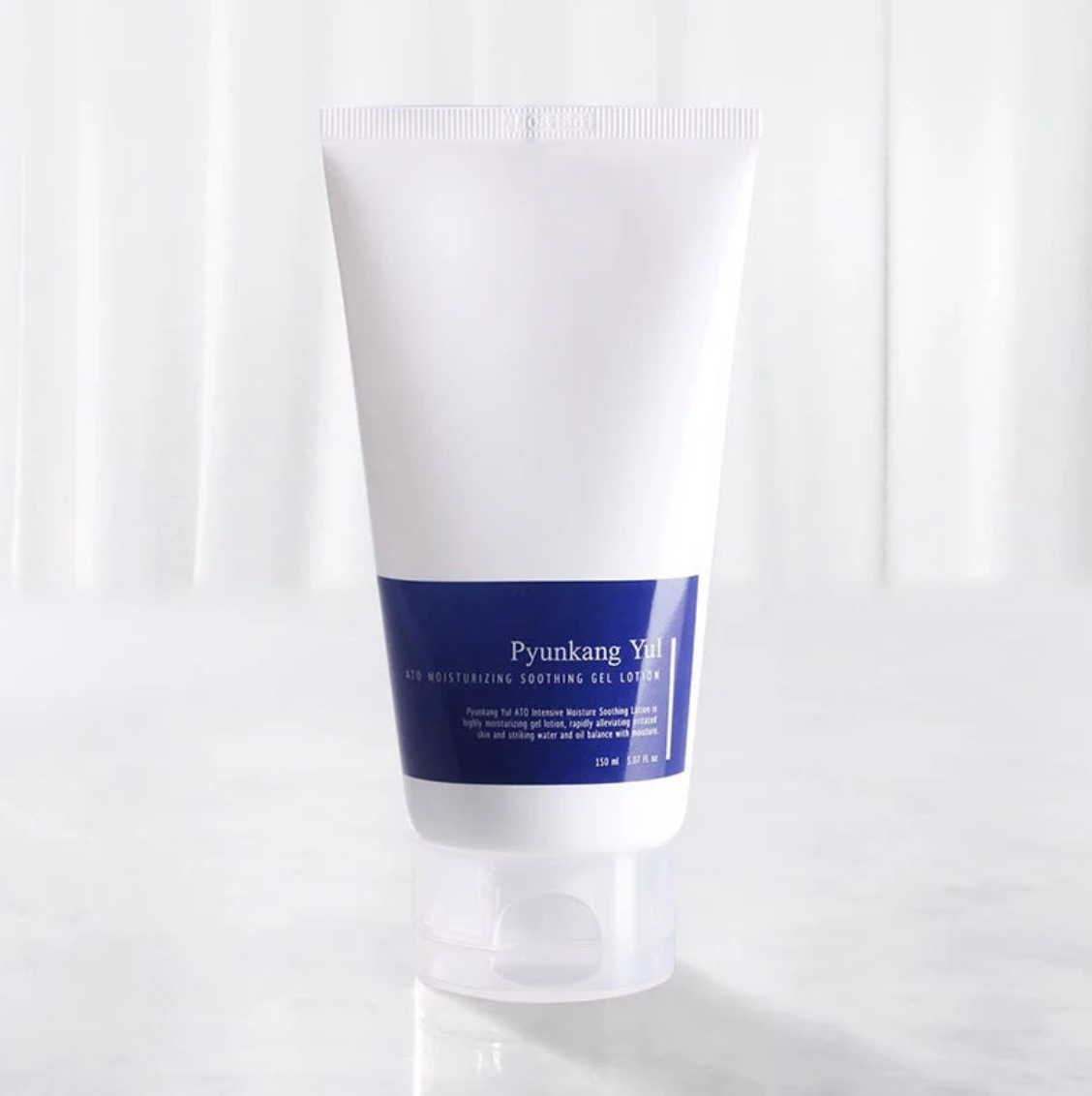 A white squeeze tube with a dark blue label band, set against a bright, softly lit white background.