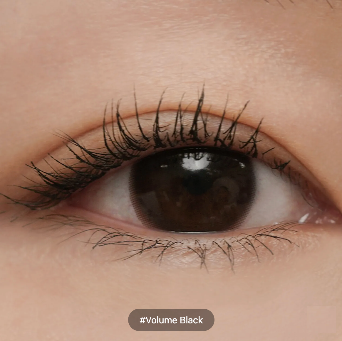 Close-up of a human eye wearing mascara that makes the eyelashes appear black and voluminous, with a text label at the bottom reading '#Volume Black'.