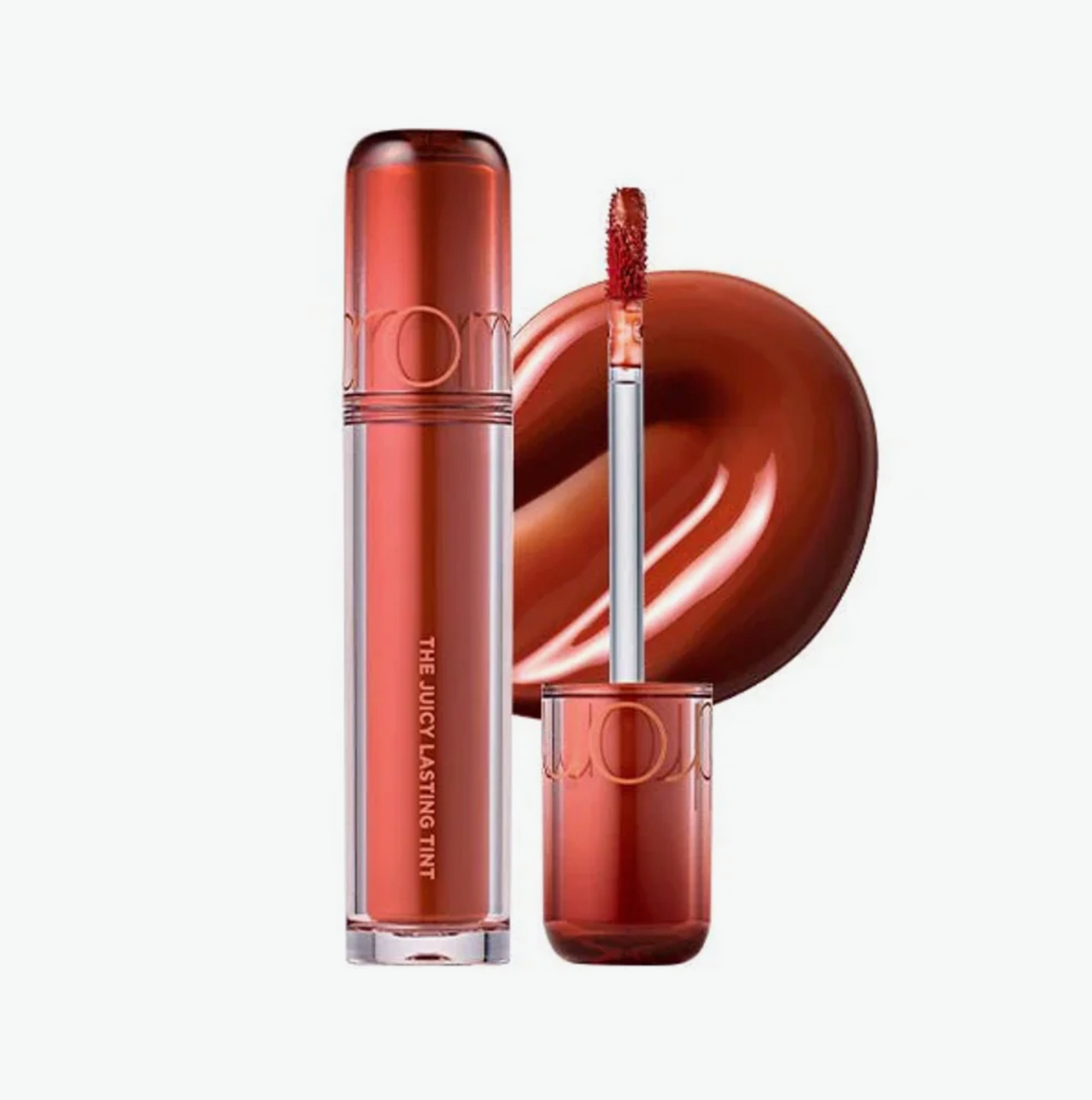 A liquid lipstick tube in a glossy coppery orange shade, shown with the applicator wand and a circular swatch of the product on a white background. The brand name 'rom' is visible on the packaging.