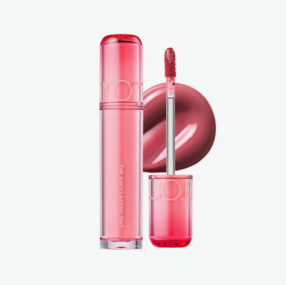 A pink liquid lipstick tube and its applicator wand are shown on a clean white background, alongside a circular swatch of the lipstick color.