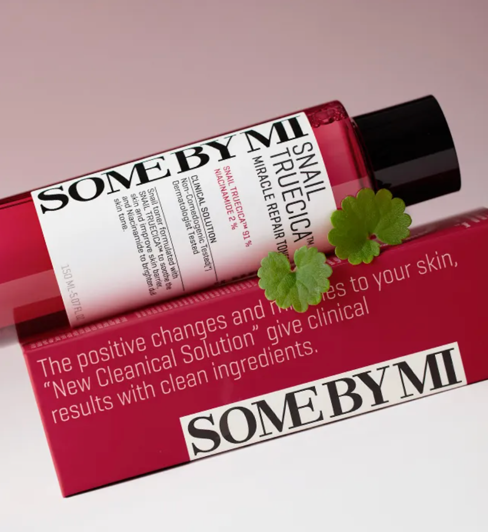 A red squeeze bottle labeled SOME BY MI Trucial True Cica with a black cap, resting on top of a matching red box. A small green leafy sprig is placed in front.