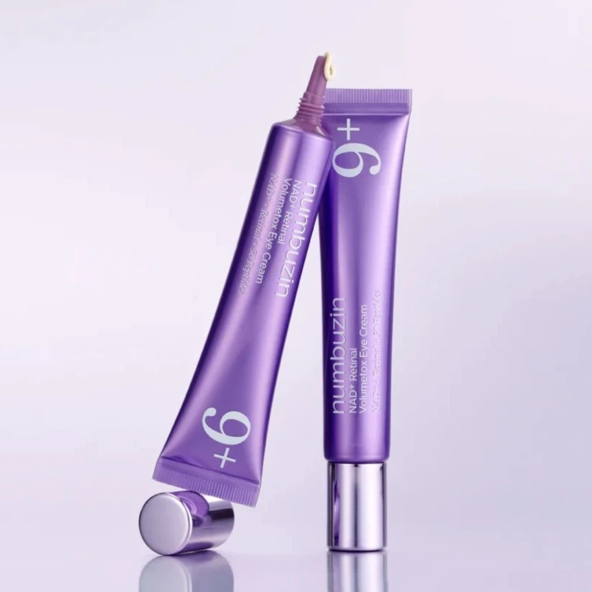Two purple tubes of numbuzia +9 Numb Relief Pain Relieving Cream, one standing upright and the other lying on its side with the cap removed, on a light gray reflective background.