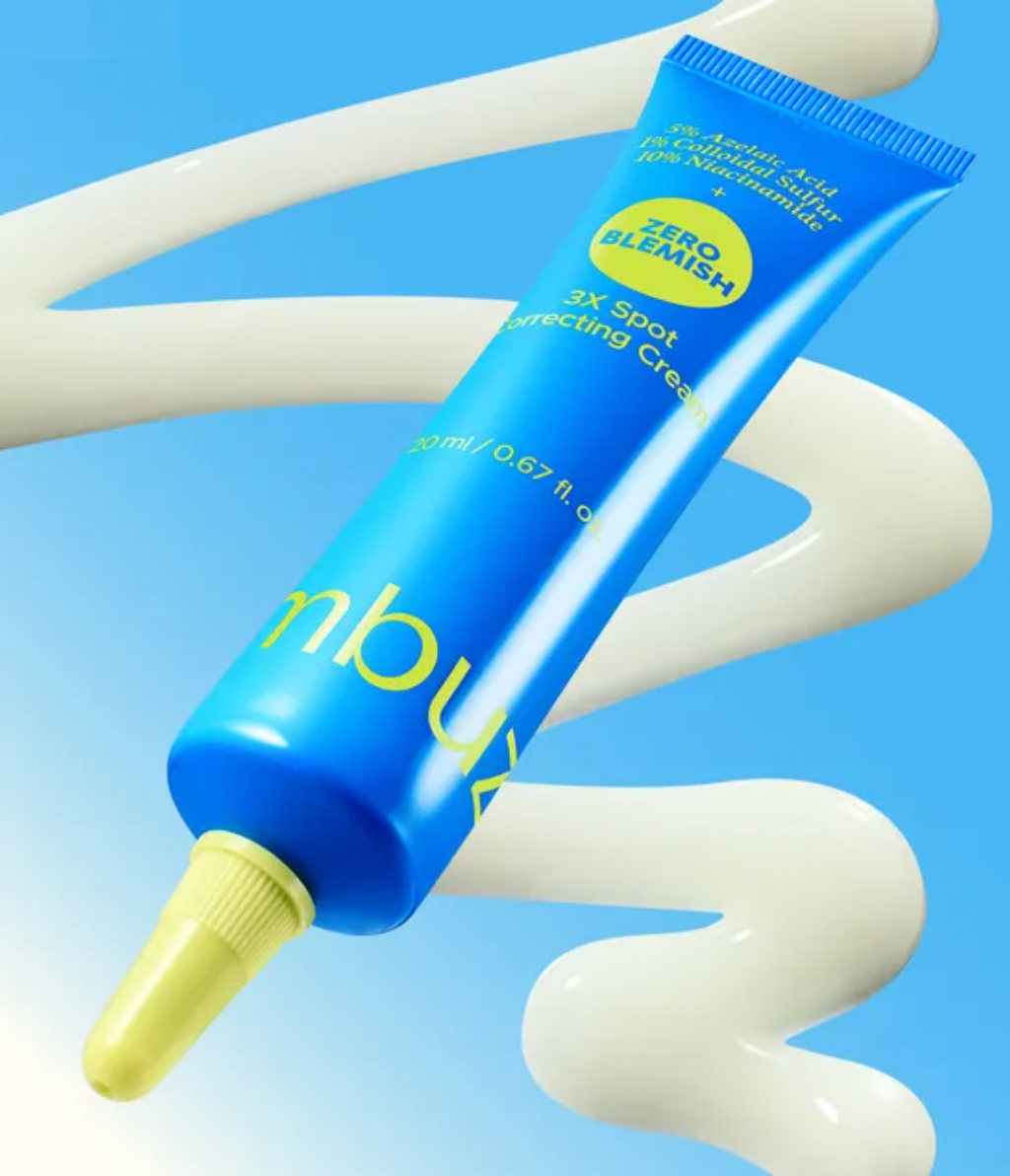A blue squeeze tube of nbux Zero Blemish 3X Spot Correcting Cream floating diagonally over a white cream swirl on a light blue background.
